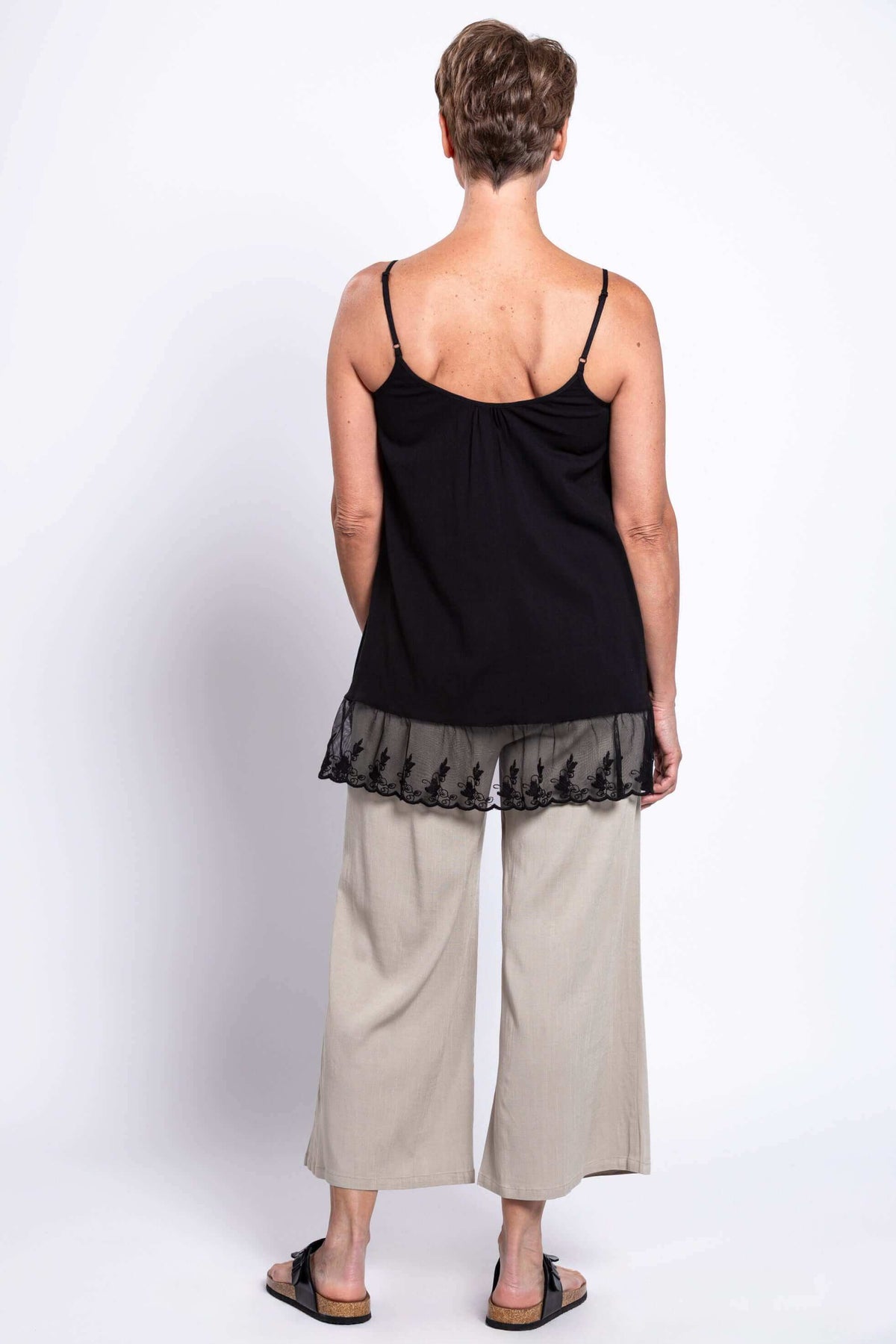 Back view of a woman in a black lace-hem tank top and beige pants