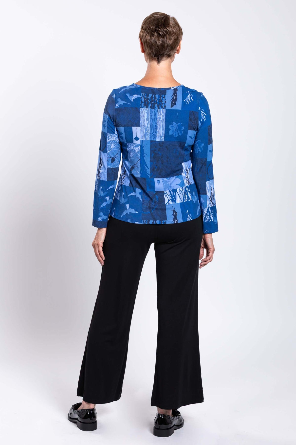 Back view of a woman modeling a blue botanical print long sleeve tee with black pants