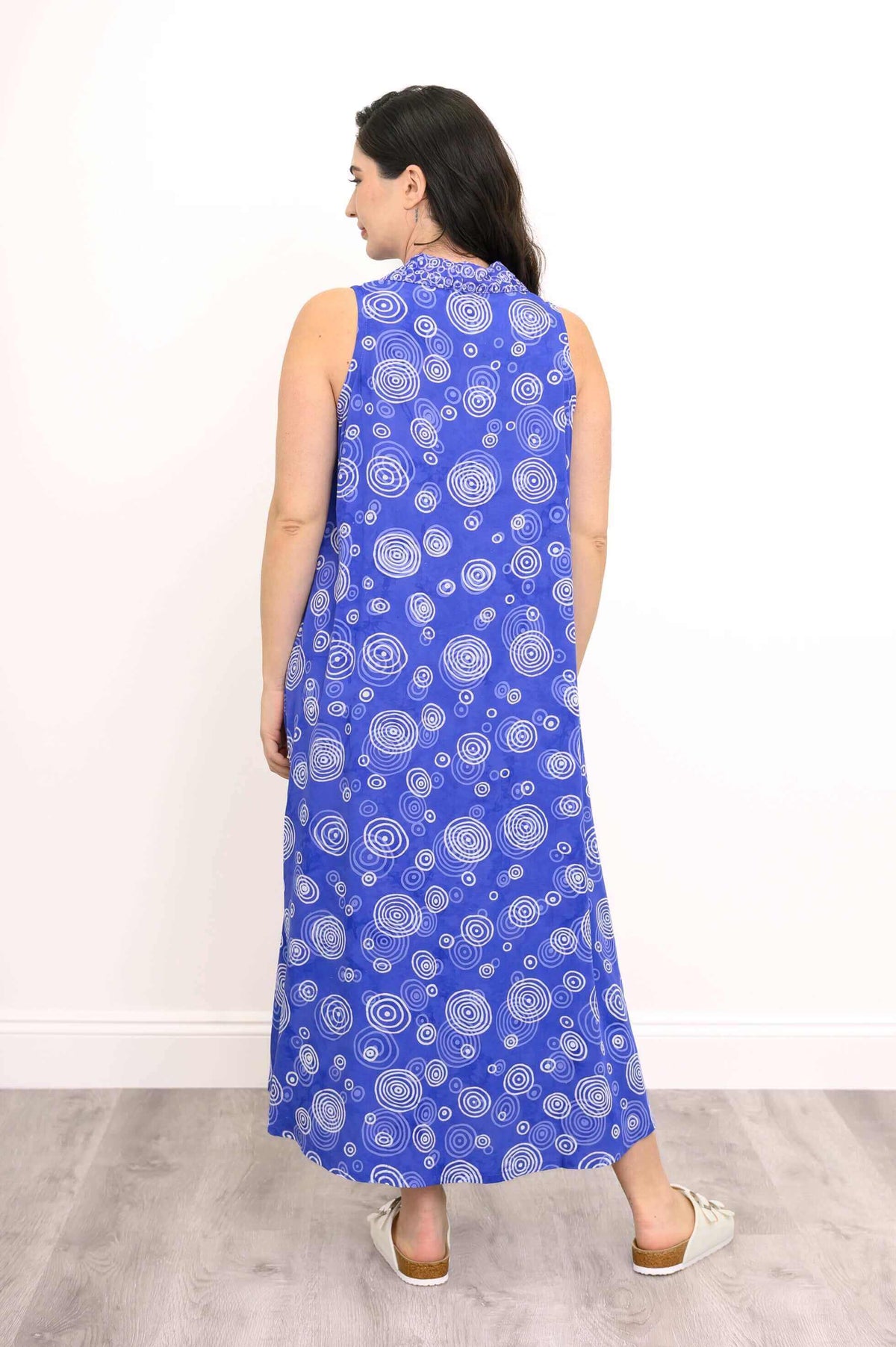 Back view of model in blue sleeveless dress with white swirl patterns
