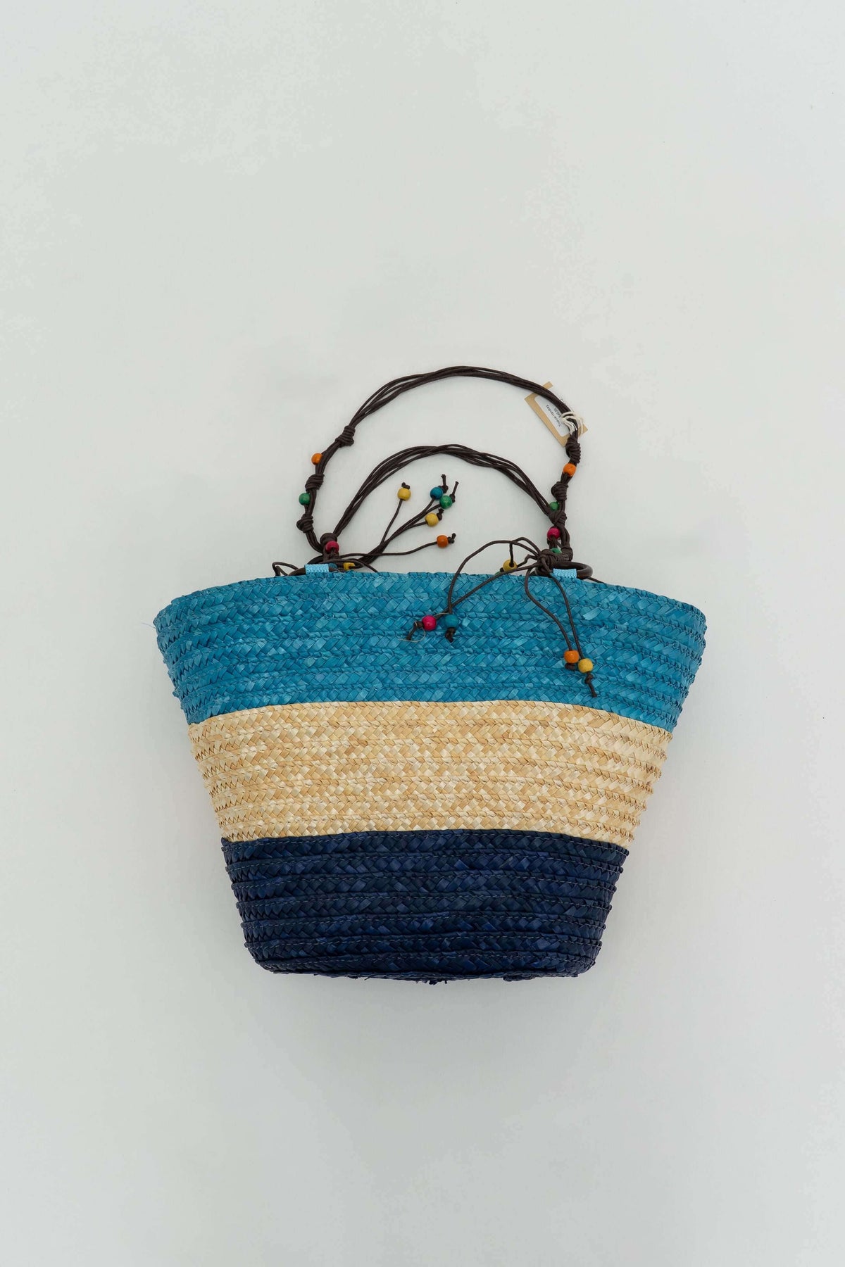 Back view of rattan tote showing blue, beige, and navy color blocking with beaded handles