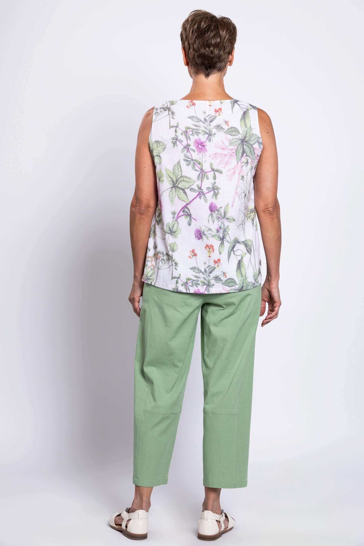 Back view of older woman in floral botanical tank top and green pants