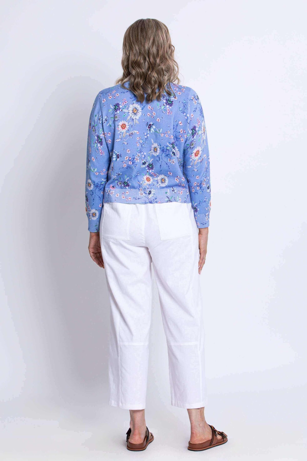 Back view of a woman in a blue floral cardigan and white pants