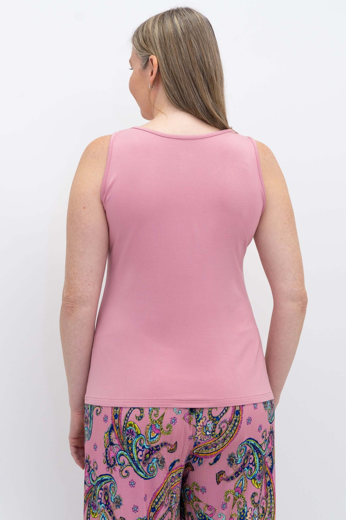 Woman wearing a pink bamboo tank top with paisley pants, back view