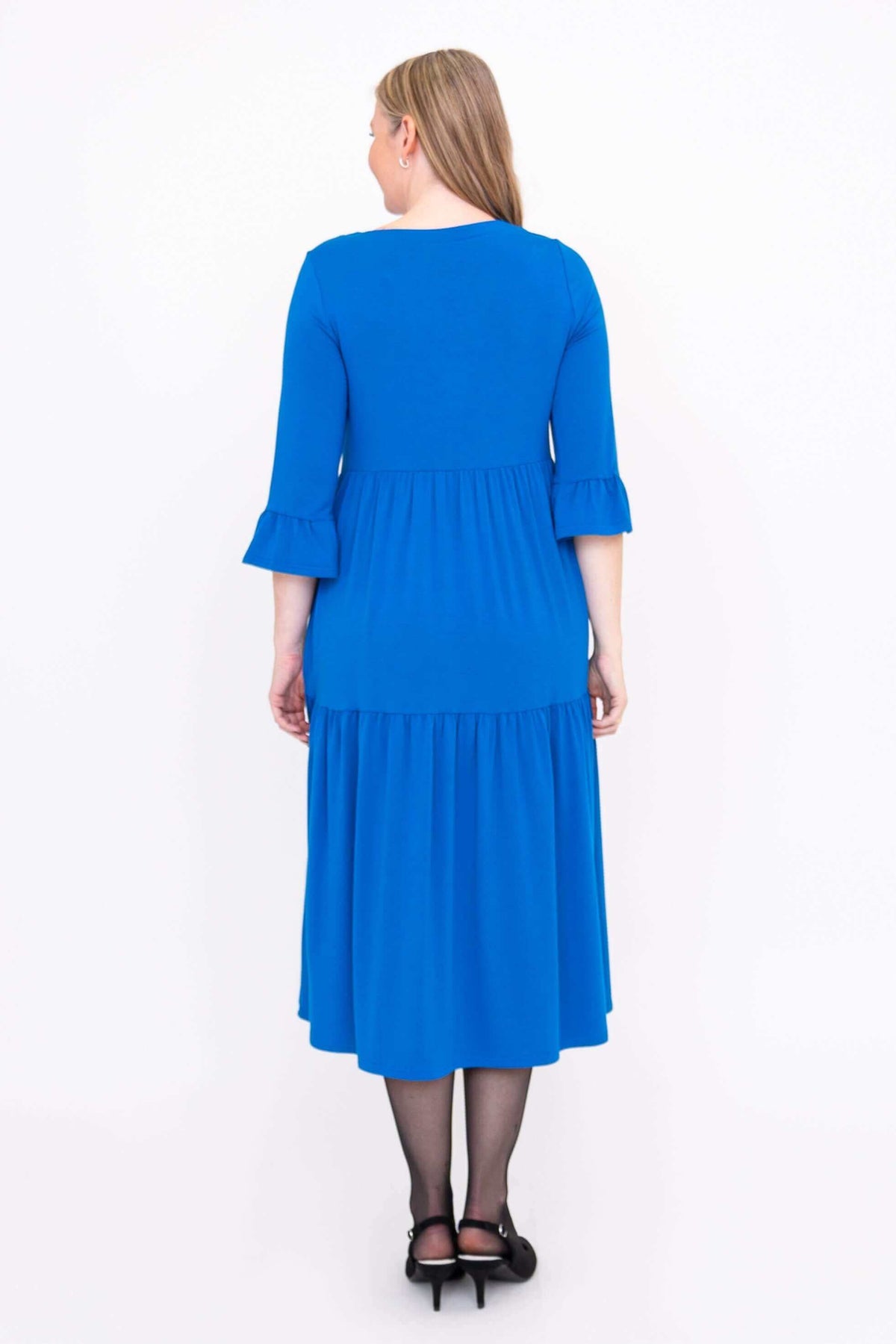 Back view of model wearing a blue tiered midi dress with 3/4 ruffle sleeves