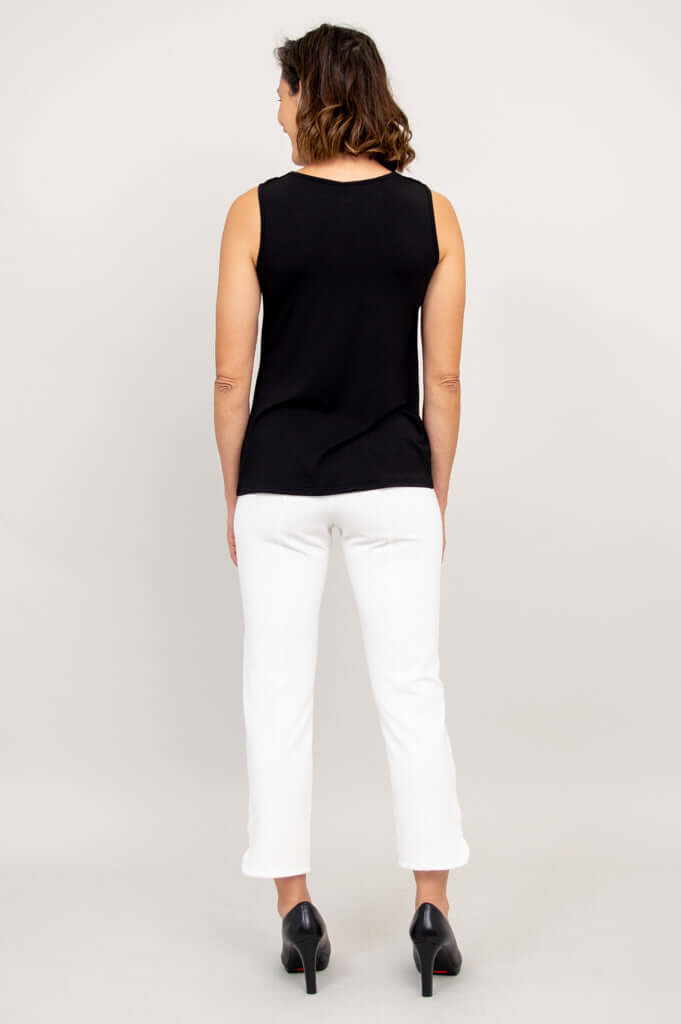 Back view of a woman wearing a black sleeveless cowl neck top with white pants