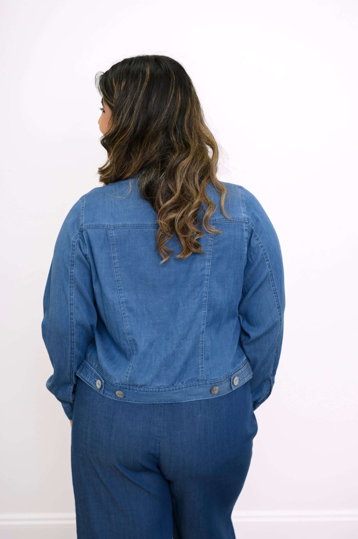Back view of a woman showcasing the blue Tencel denim jacket’s rear details.
