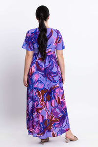 Back view of a woman in a flowing purple floral print maxi dress with short sleeves