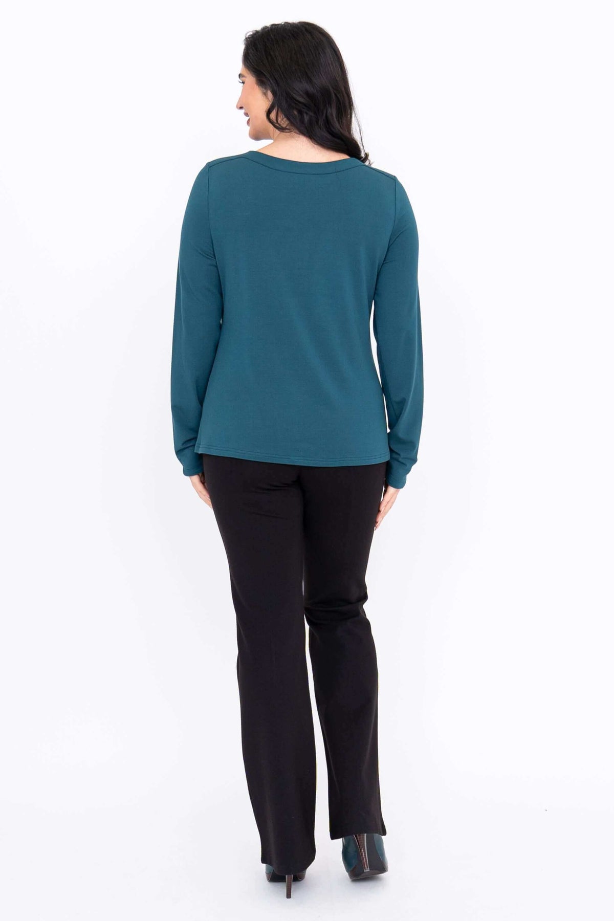 Back view of a woman in teal boat neck long sleeve top and black pants