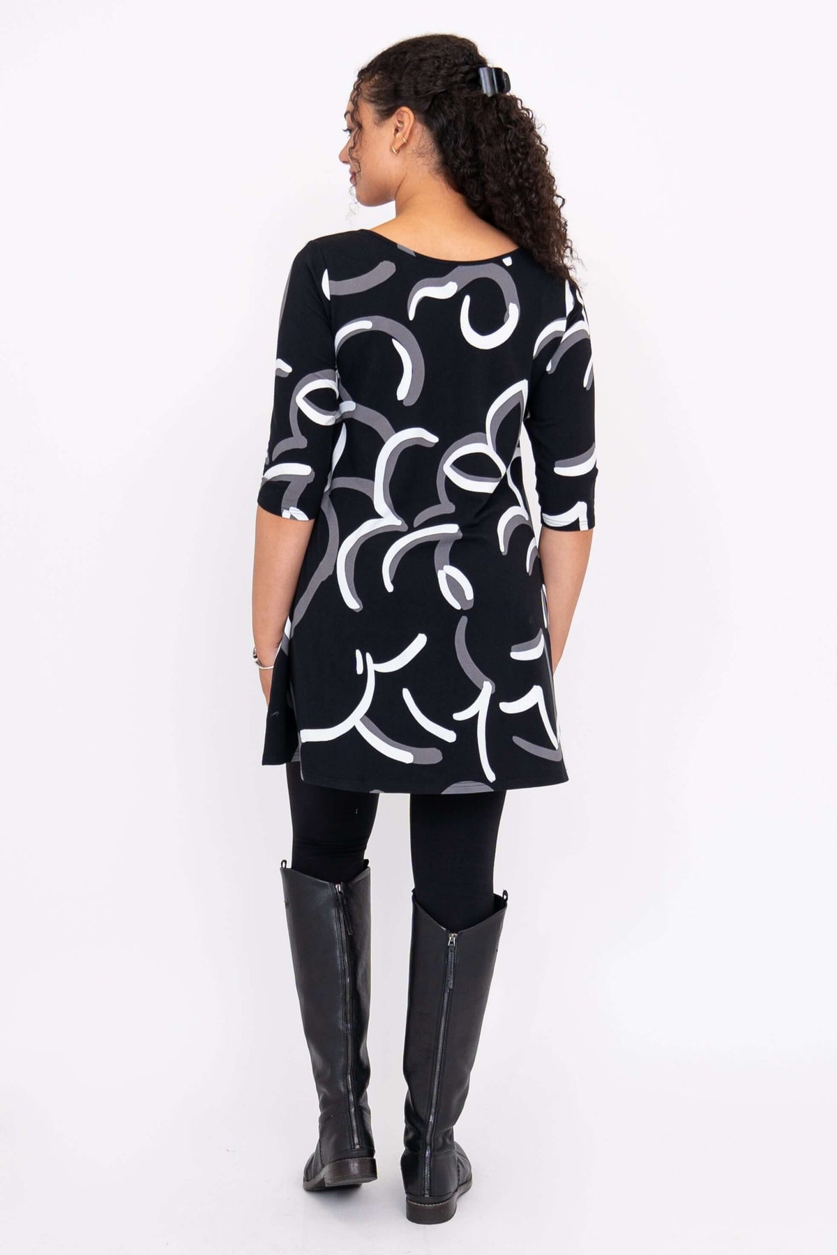 Back view of Spirit Dress, displaying abstract print and A-line silhouette, worn with leggings and boots