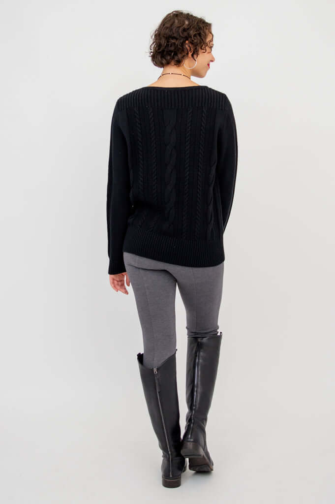Back view of a person showing the cable knit design of a black sweater paired with grey pants and boots