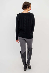 Back view of a person showing the cable knit design of a black sweater paired with grey pants and boots