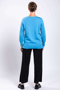 Back view of woman wearing blue V-neck cotton sweater and black pants