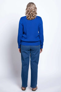 Back view of woman wearing blue cable knit sweater and blue jeans, hair styled in waves