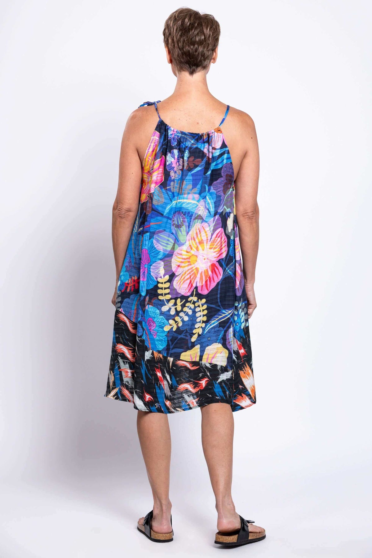 Back view of a woman in a breezy, colorful floral sleeveless dress with tie shoulder detail