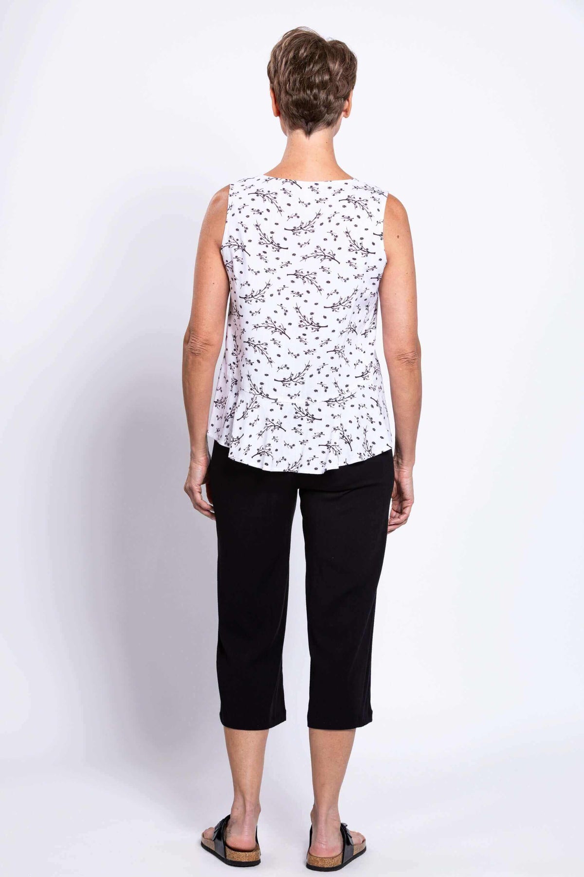 Back view of woman in white floral peplum tank and black pants