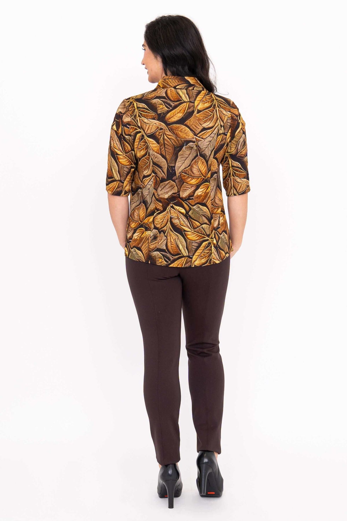 Back view of model wearing a golden leaf print blouse with brown trousers