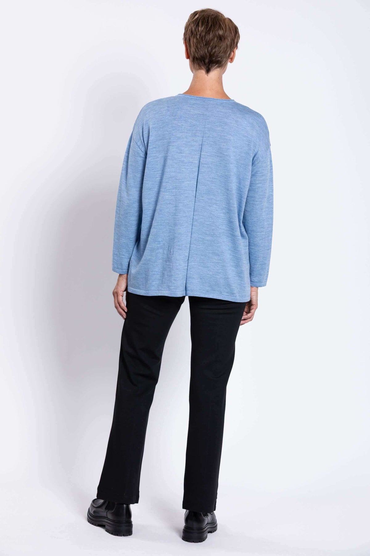 Back view of a woman showing the detail of a light blue knit sweater with black pants