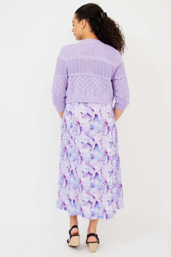 Back view of woman wearing lilac pointelle cropped cardigan over purple dress