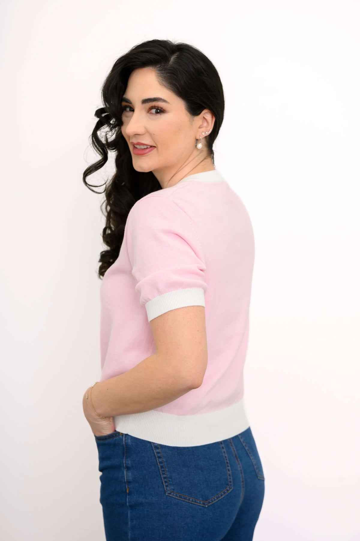 Back and side view of a woman in a pink two-tone cardigan and blue jeans