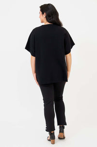 Back view of woman in black short-sleeve cotton cardigan and slim black pants