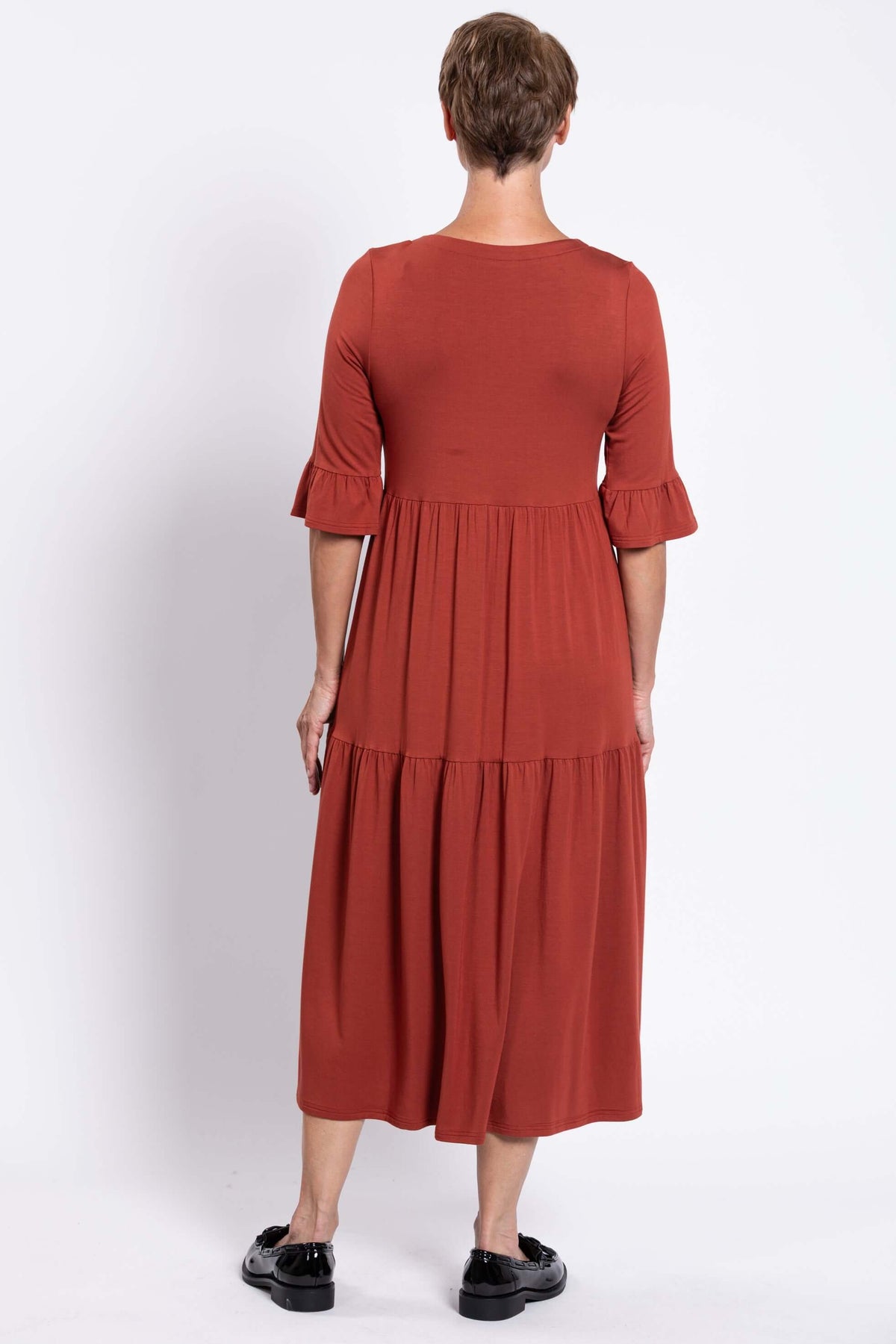 Back view of model showing rust-colored tiered midi dress with ruffle sleeves