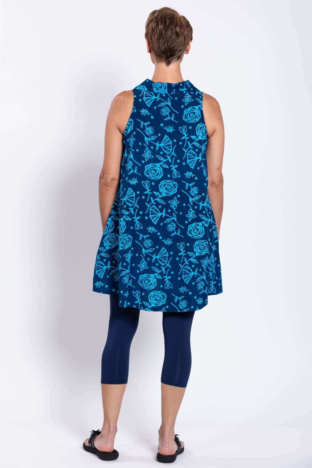 Back view of blue A-line swing tank dress with all-over floral pattern, worn over navy leggings