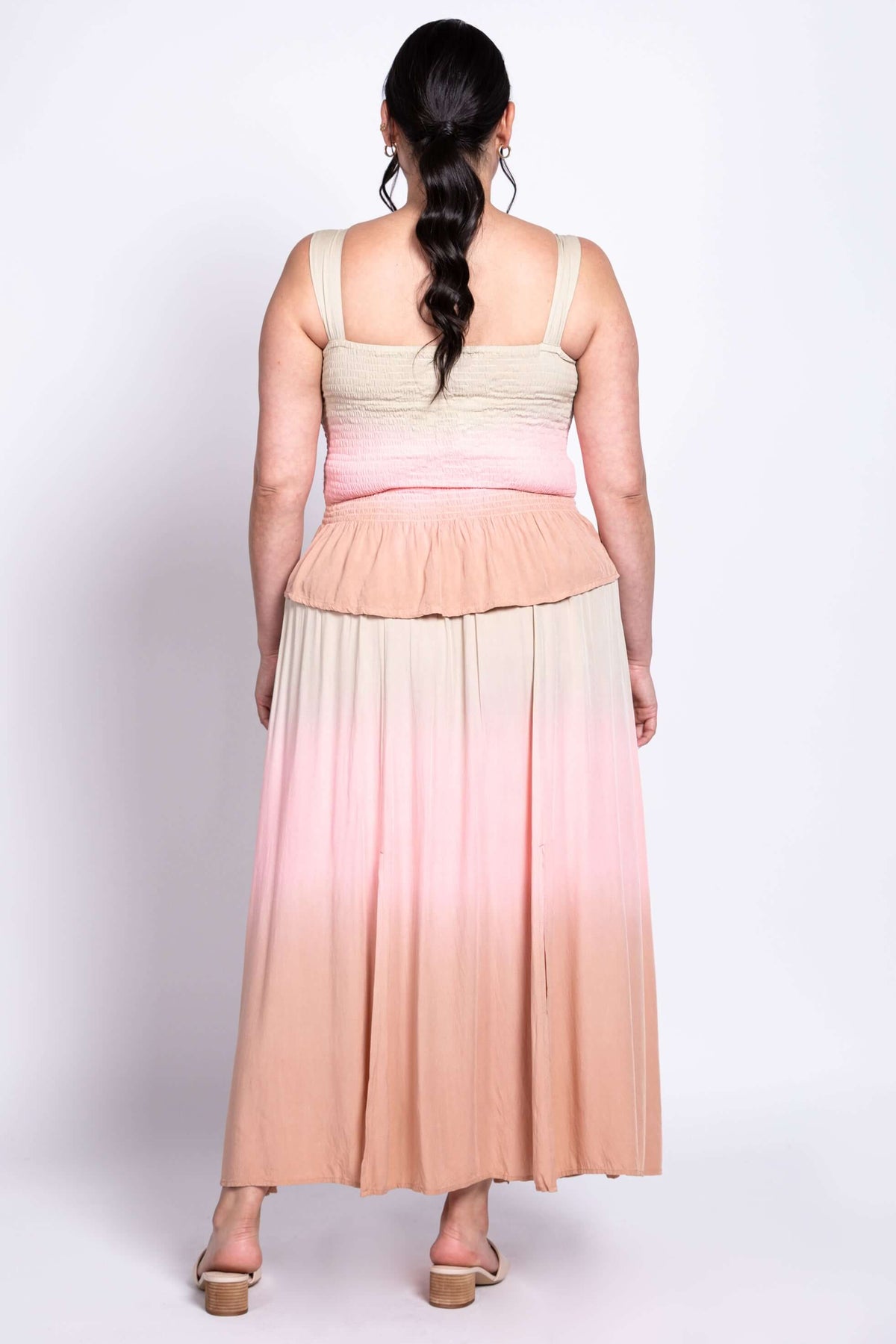 Back view of a woman wearing a maxi dress with beige, pink, and peach ombre gradient