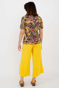 Back view of woman in botanical print tee and yellow pants, showing back details of the top