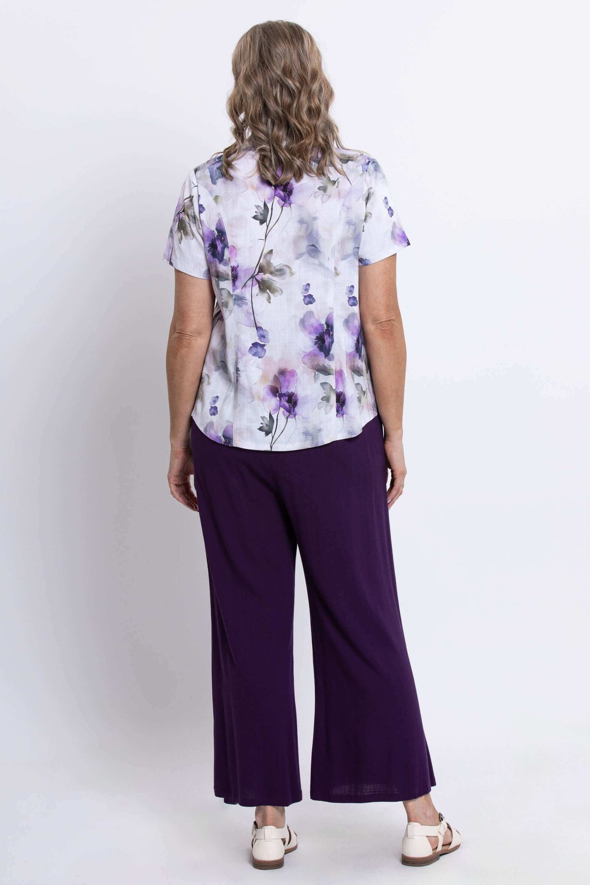 Back view of a woman wearing a floral button-up shirt and purple wide-leg pants
