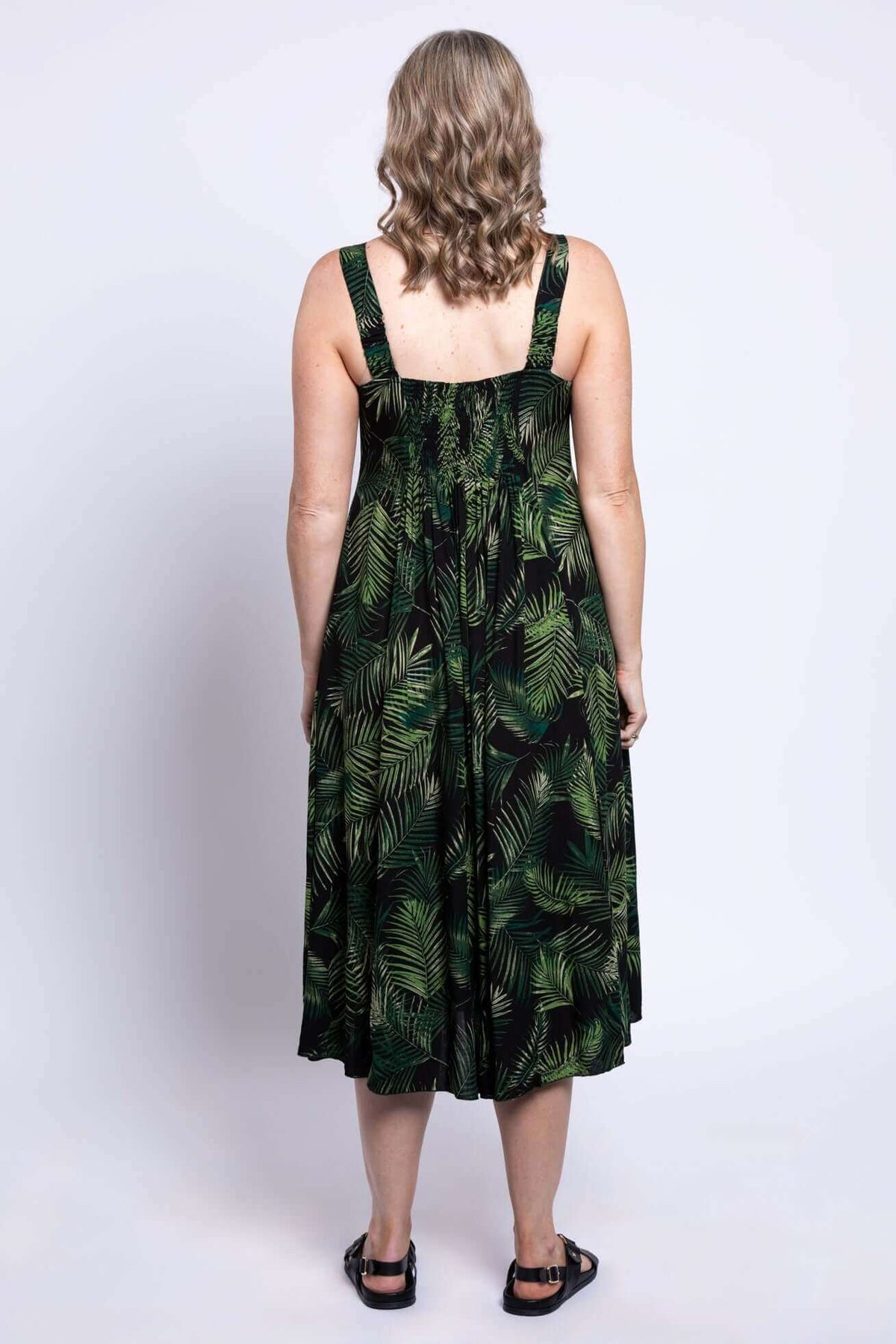 Back view of a woman wearing a sleeveless green leaf print midi dress with shirred bodice