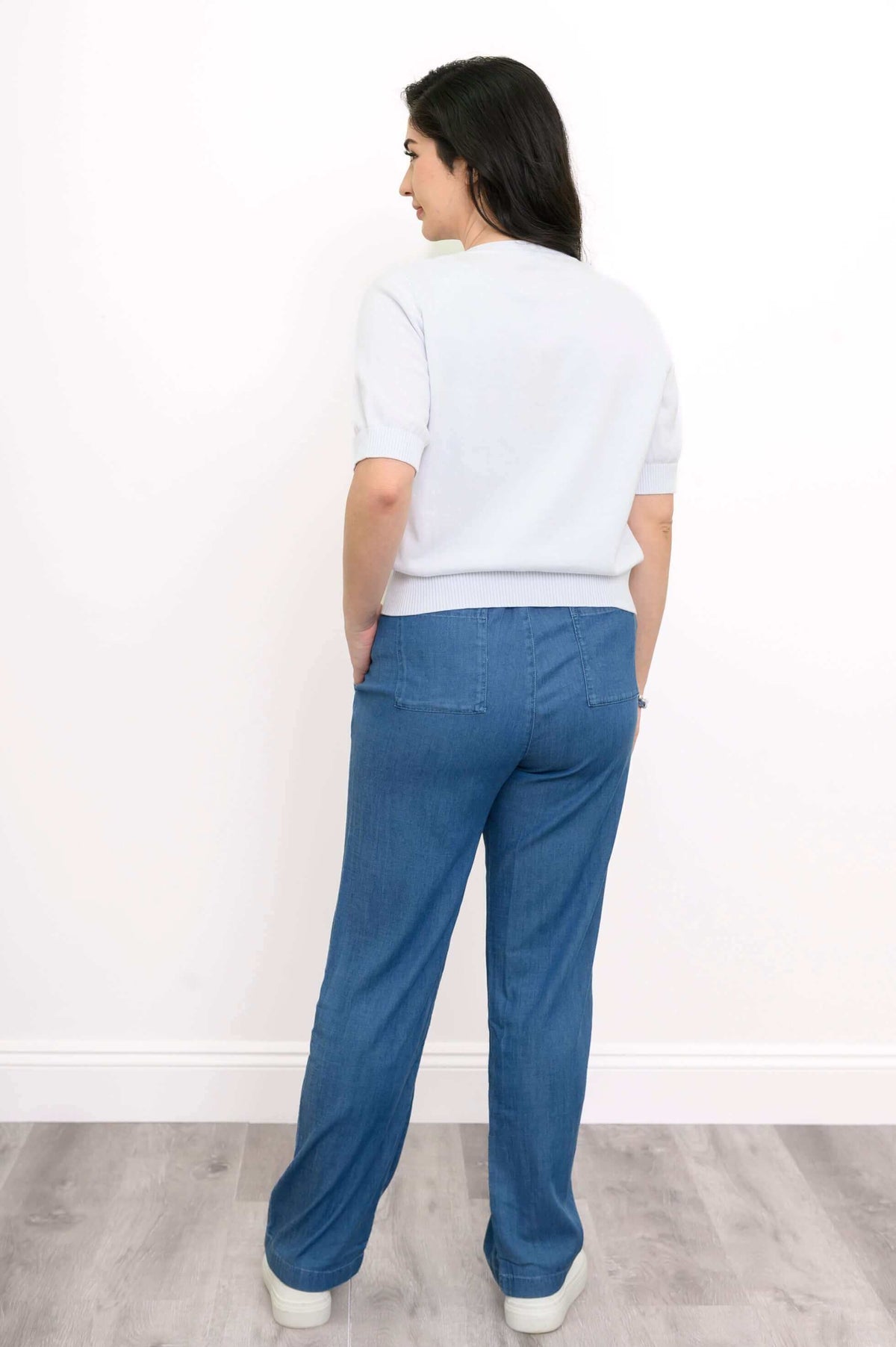 Back view of a woman in a white short-sleeve cardigan with blue pants