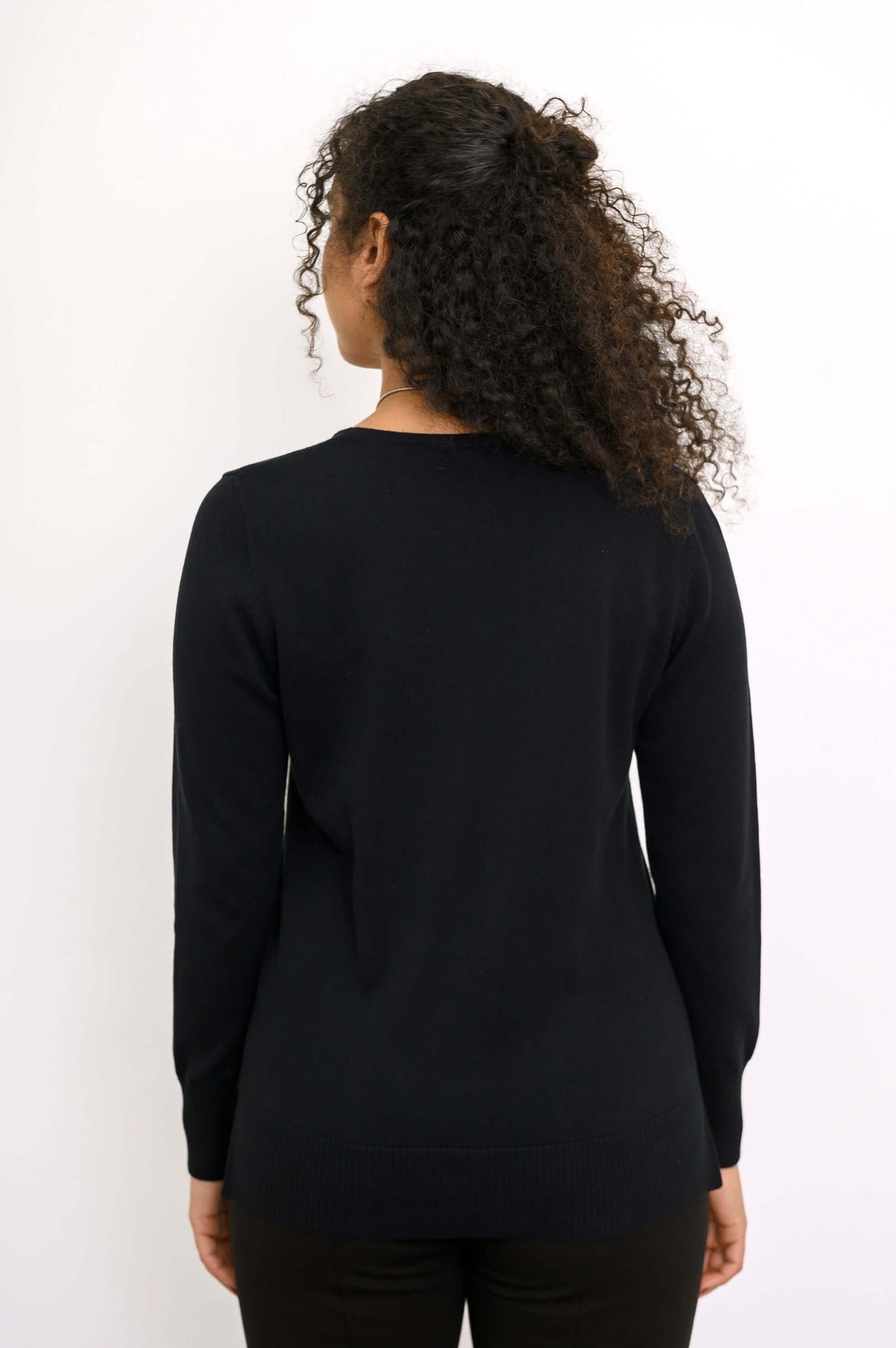 Back view of woman wearing a black V-neck black sweater with ribbed cuff and hem