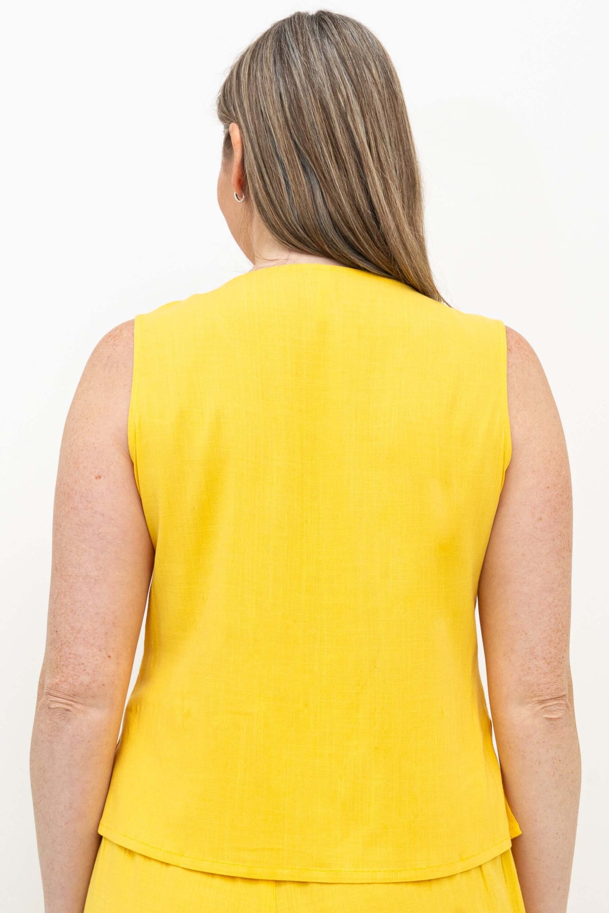 Back view of a woman wearing a yellow sleeveless cropped tank top