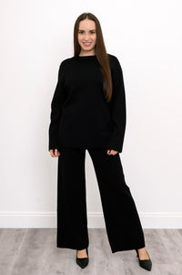 Smiling woman wearing onyx straight-leg trousers, a matching dark long-sleeve knit top, and elegant black heels.
