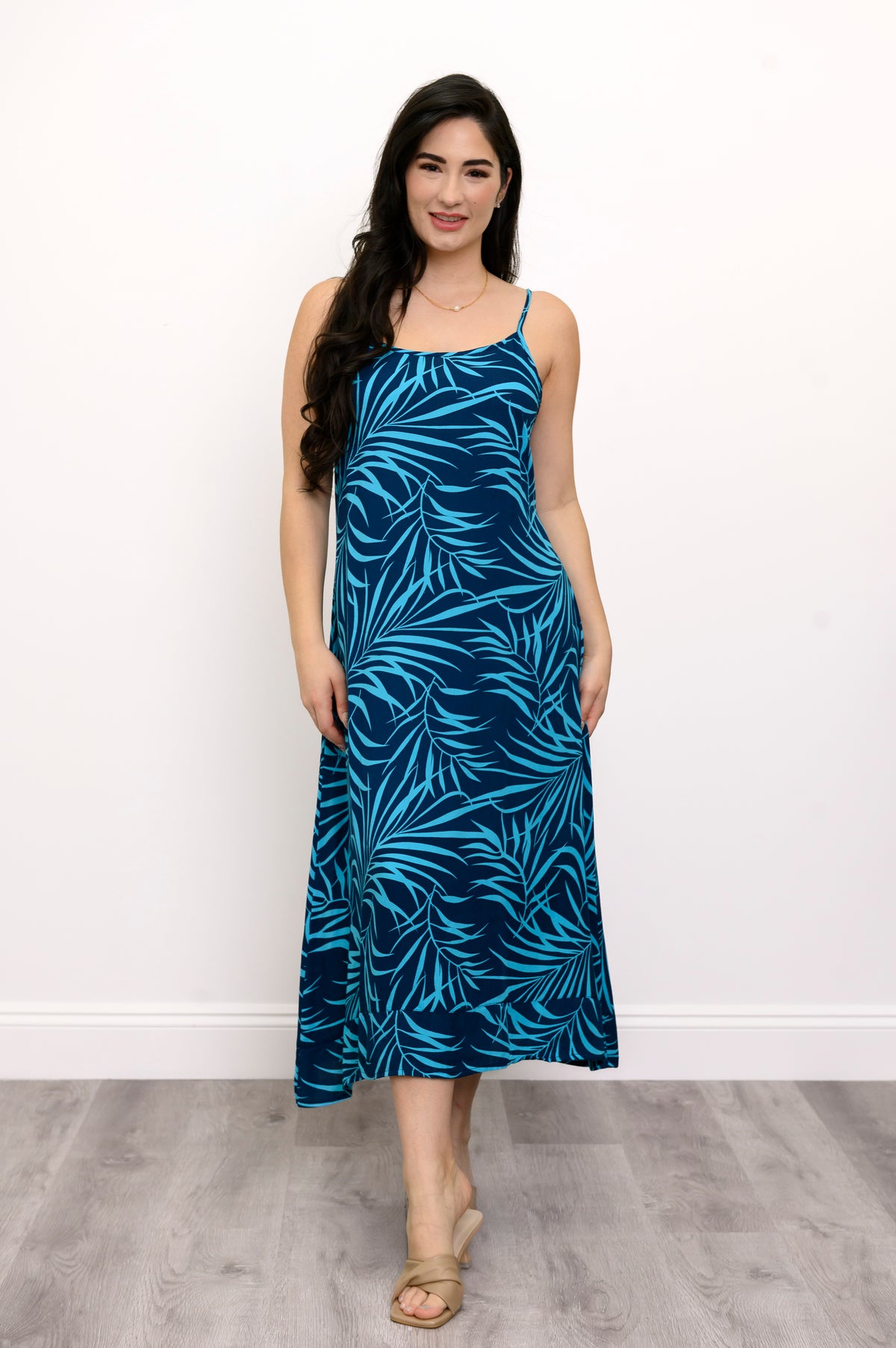 Front view of woman wearing a blue leaf-patterned dress and beige sandals against a white background
