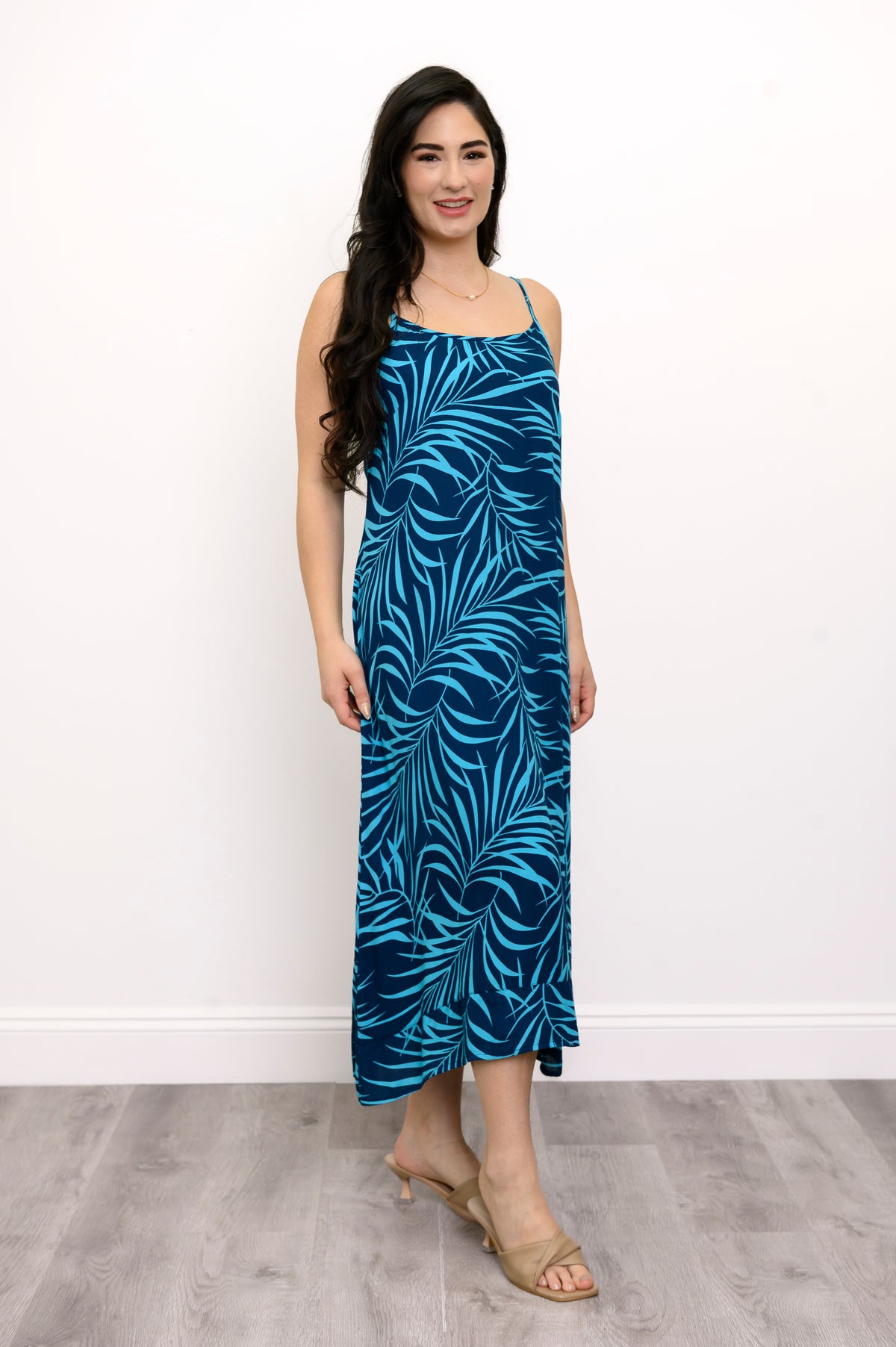 Side view of woman wearing a blue leaf-patterned dress and beige sandals against a white background