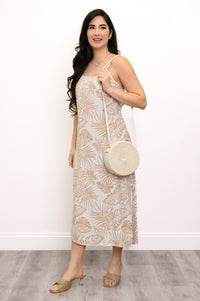 Front view of woman wearing a white and beige leaf-patterned dress and white bag against a white background