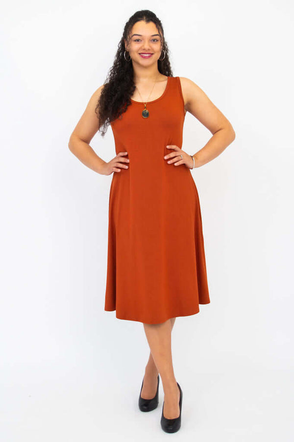 Woman modeling the Becca dress in burnt orange, hands on hips, A-line silhouette visible