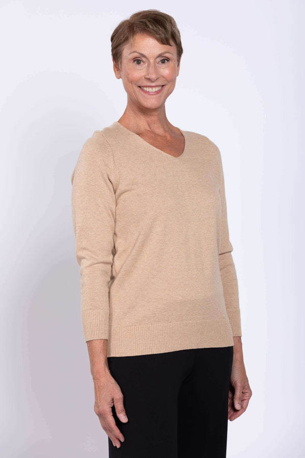 Woman wearing a beige V-neck cotton sweater with black pants, facing forward