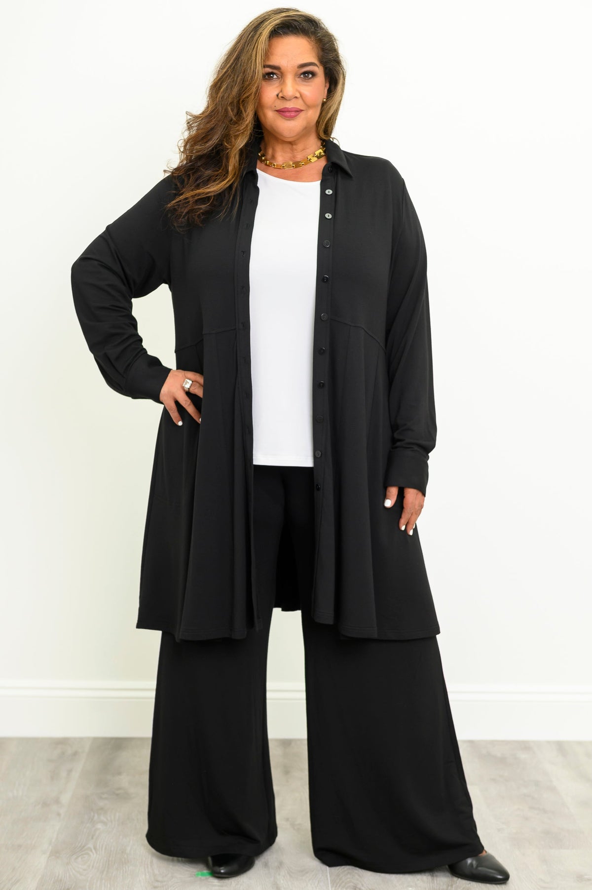 Woman wearing a black structured long tunic top with a front button placket over a white shirt and black pants