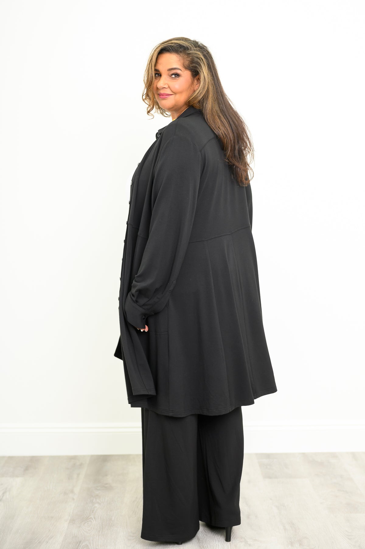 Back view of a structured black long sleeve tunic top showing a clean paneled finish across the midsection.
