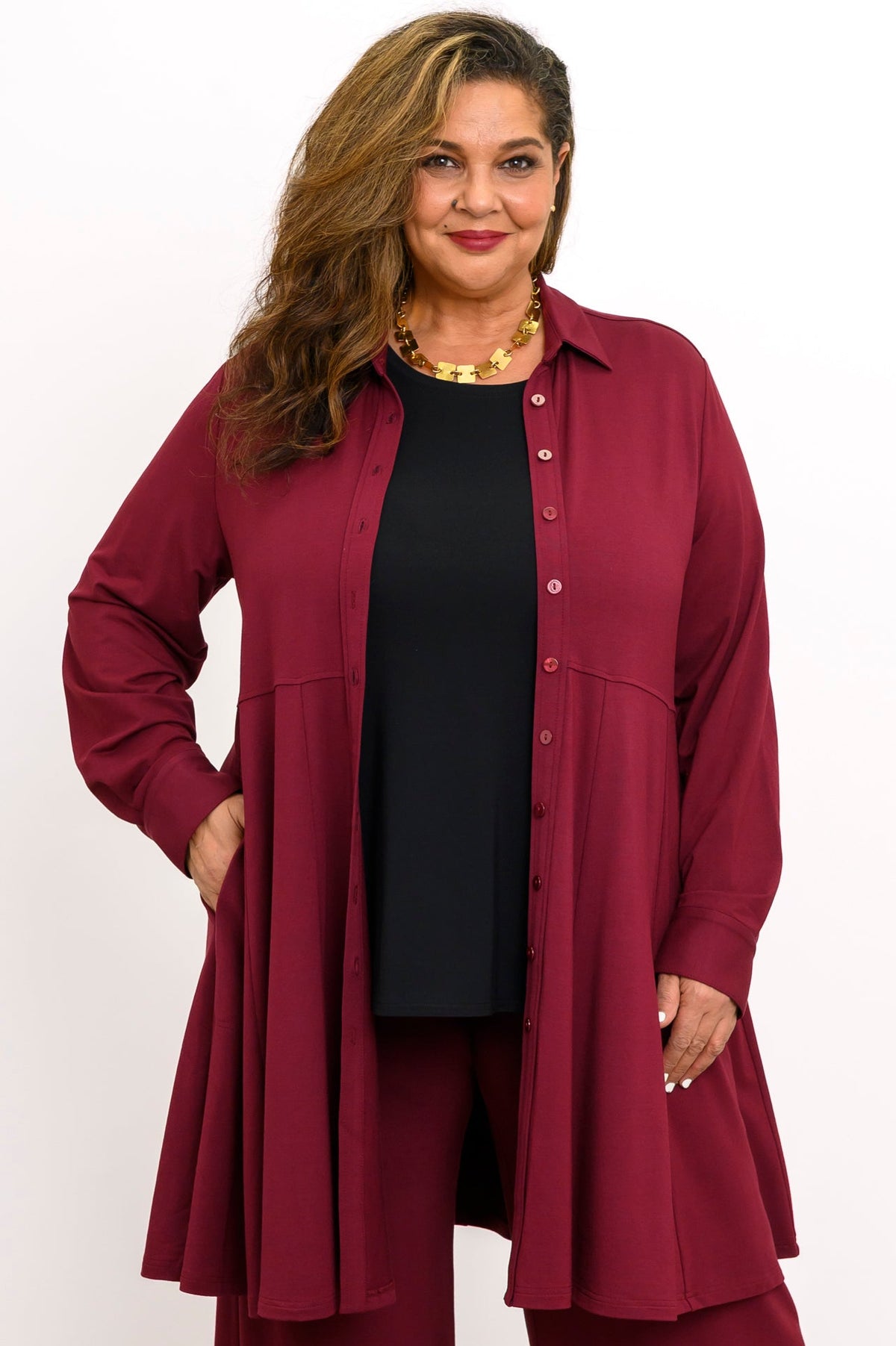 Front view of a woman wearing an open burgundy French terry button-down tunic shirt layered over a black top.