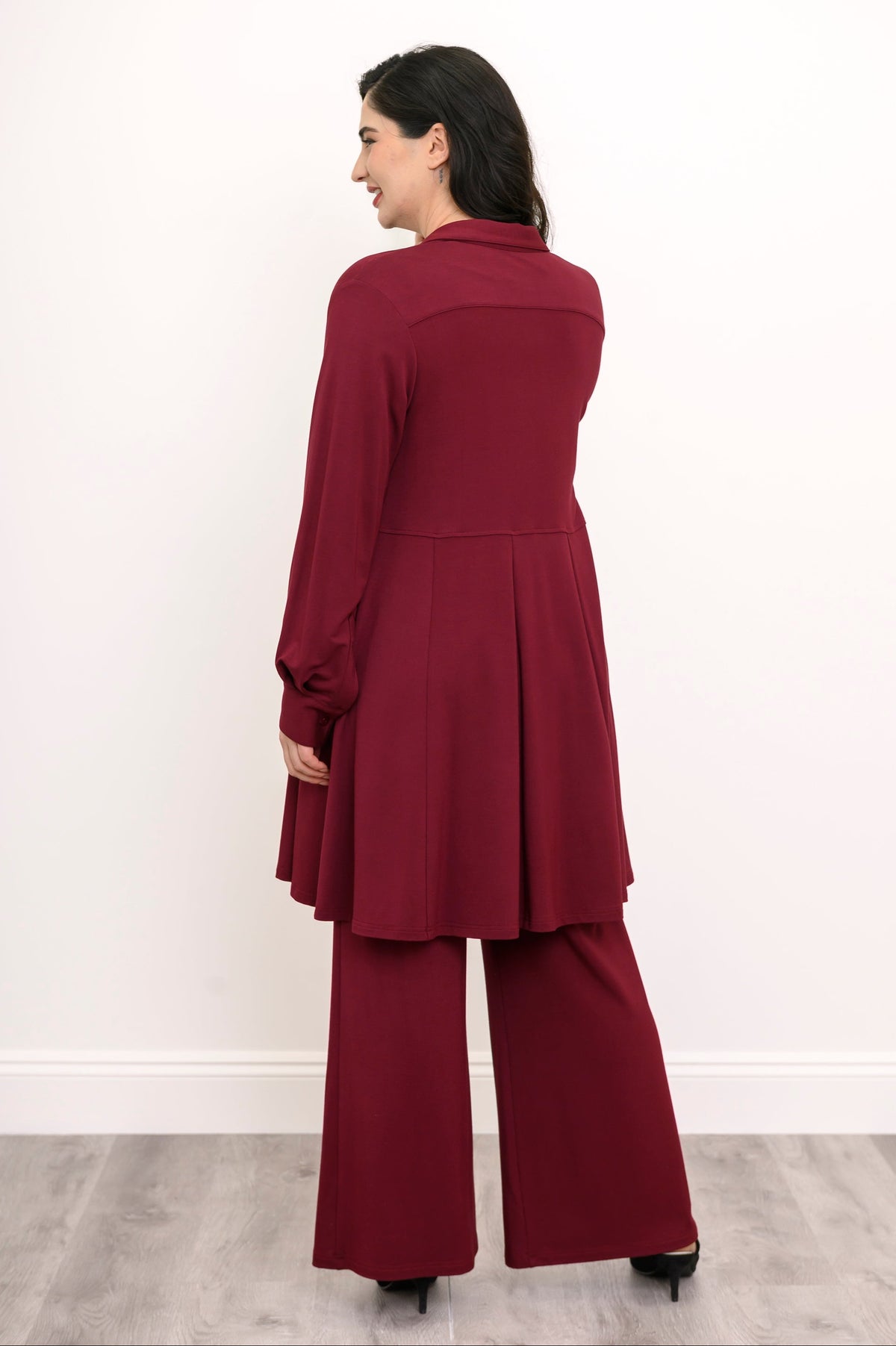 Back view of a woman wearing a structured burgundy French terry tunic shirt with matching wide-leg trousers.