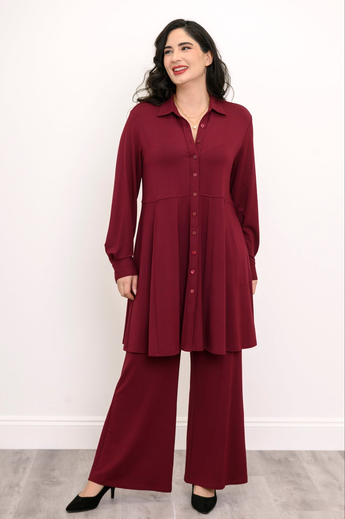 Front view of a woman wearing an open burgundy French terry button-down tunic shirt layered over a black top.