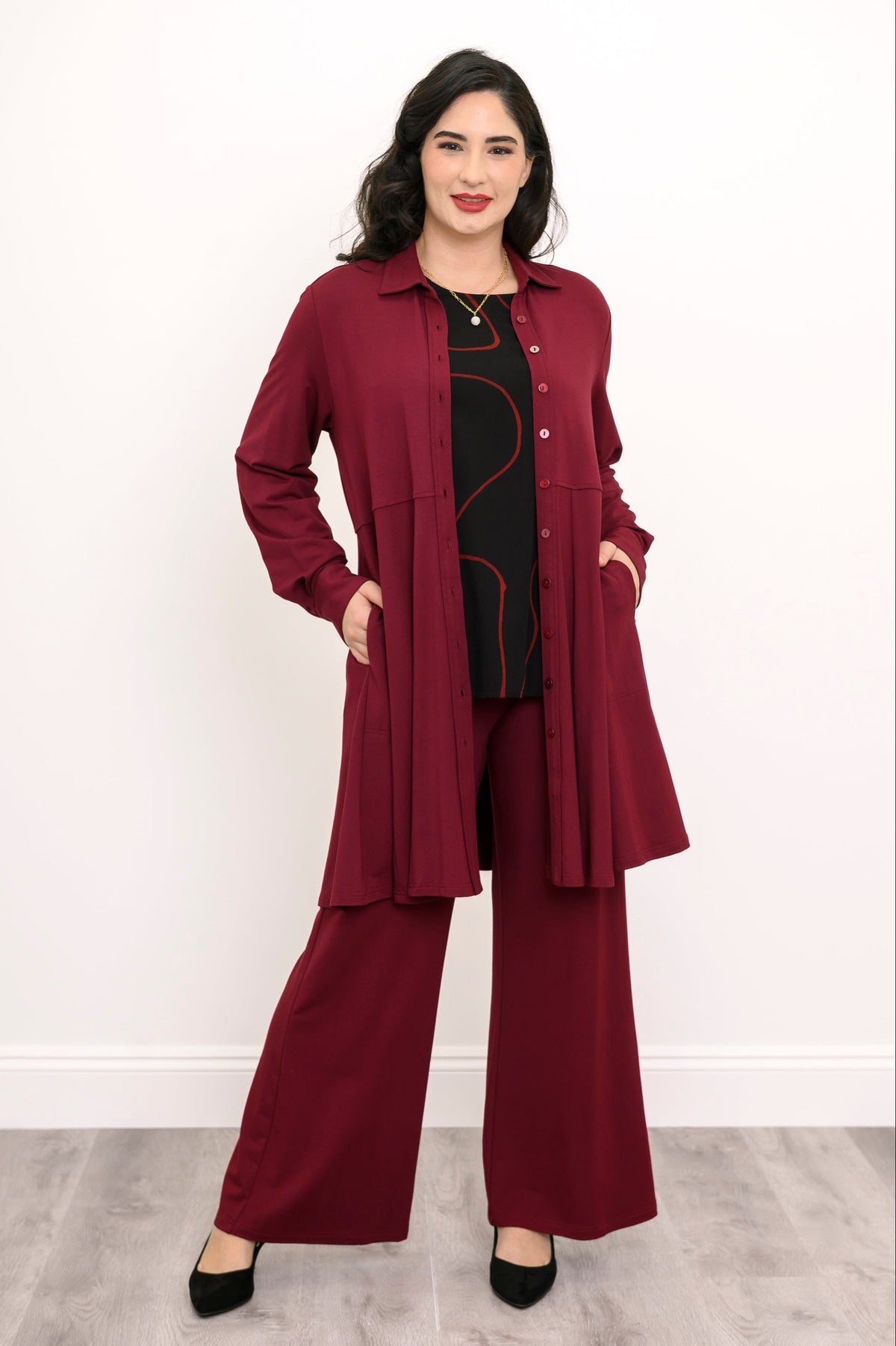 Straight-on full body portrait of an elegant women's burgundy long-sleeve knit tunic shirt with cuffed sleeves.