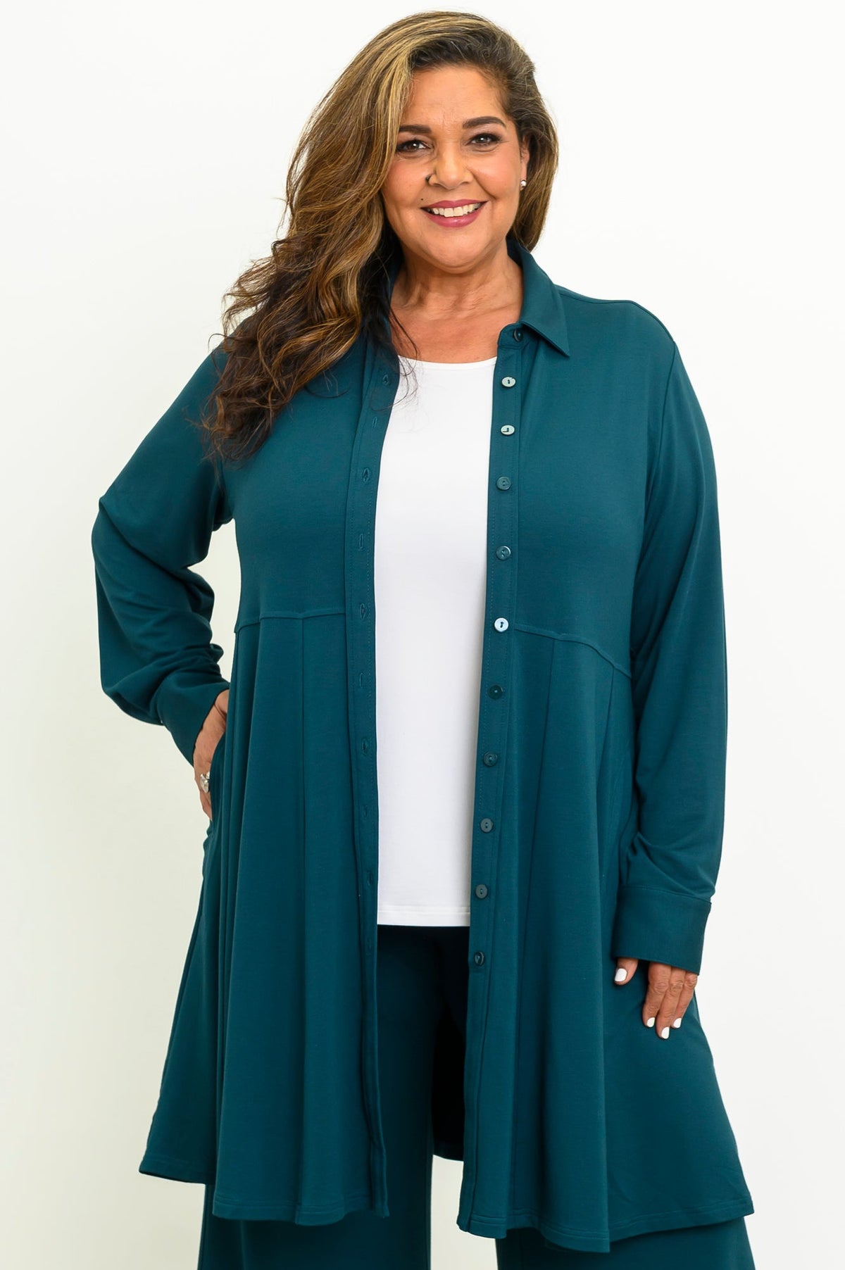 Front view of a woman wearing an open crystal teal French terry tunic shirt layered over a white top.