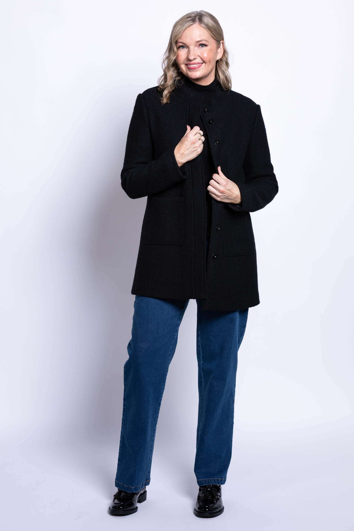 Woman showing black boiled wool coat partially open over jeans and a turtleneck