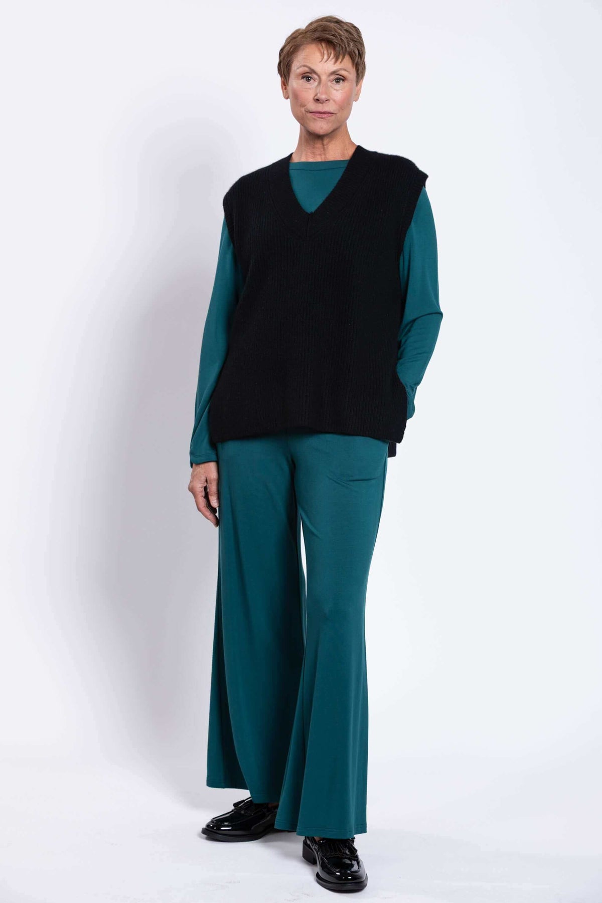 Woman posing in black boxy vest and teal flared pants, front angle