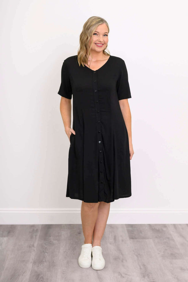 Woman wearing a black button-up dress with short sleeves and pockets, front view