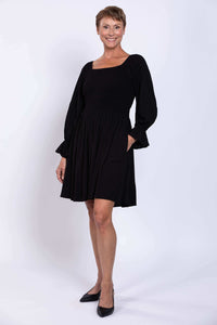 Woman wearing a black dress with shirred bodice, square neckline, and ruffled sleeves